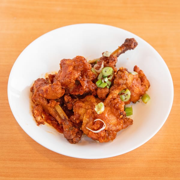 A white plate filled with crispy, saucy chicken lollipops garnished with sliced green onions.