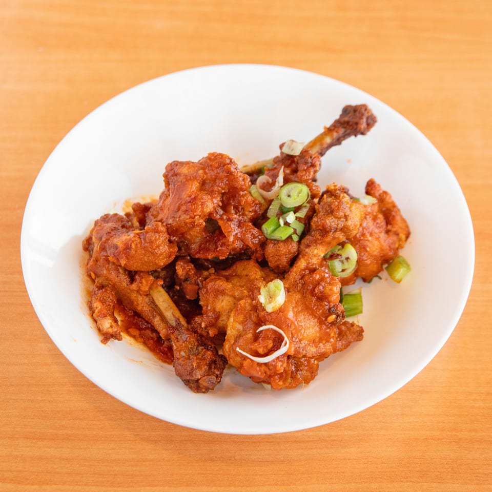 A white plate filled with crispy, saucy chicken lollipops garnished with sliced green onions.